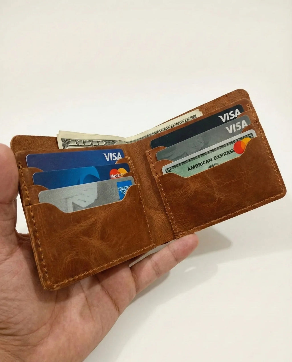 Brown leather wallet with cards and money held by a hand on a white background
